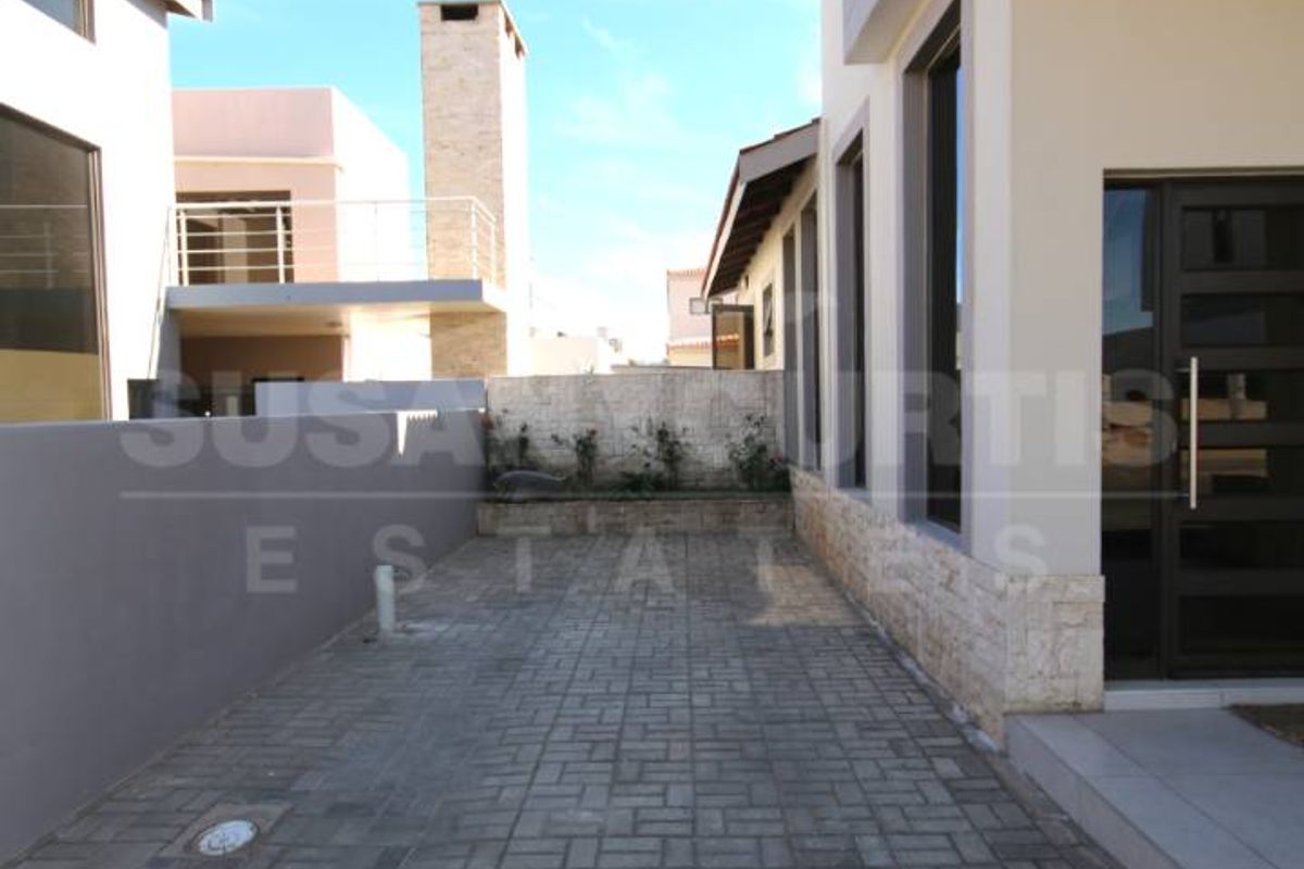 A paved rear exterior area featuring stone cladding accents, a prominent external chimney, and a balcony overlooking the side passage.