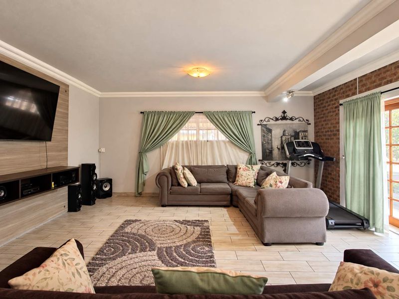 Spacious living room featuring tiled flooring, crown molding, an exposed brick feature wall, and a built-in media console with direct access to the outdoors.