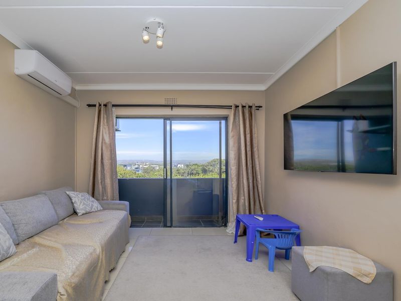 A comfortable living room featuring an air conditioning unit, coved ceilings, and sliding glass doors that open to a balcony with scenic views.