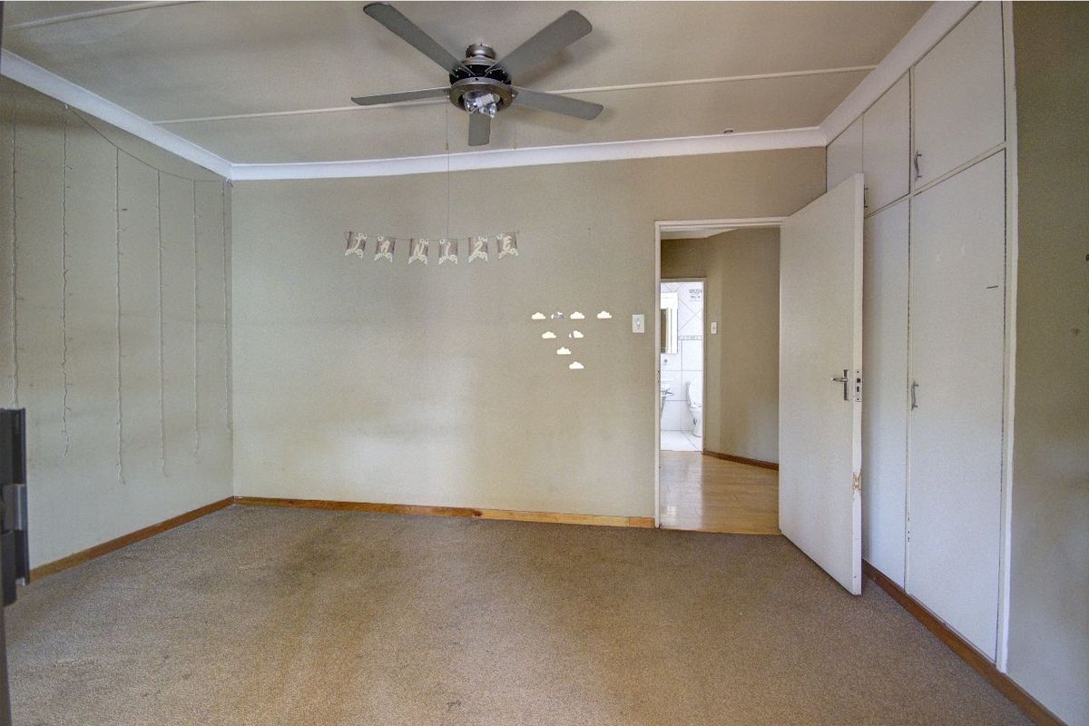 A spacious bedroom featuring built-in cupboards, a ceiling fan, and direct access to an en-suite bathroom.