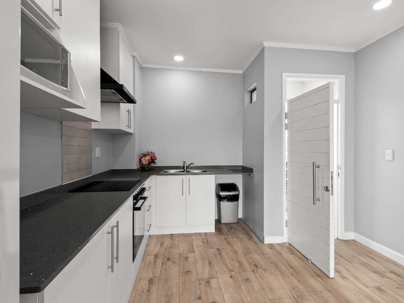 Modern kitchen featuring white cabinetry, dark laminate countertops, integrated appliances, and wood-look laminate flooring in a clean, well-lit space.