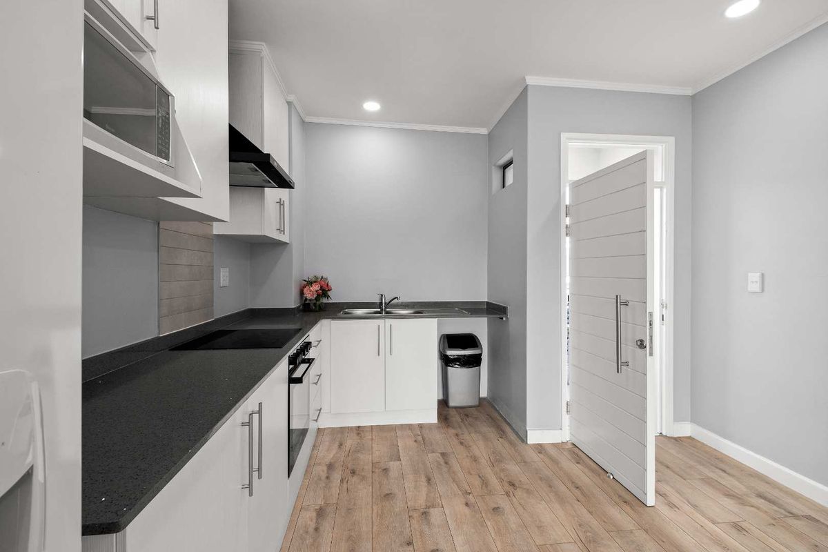 Modern kitchen featuring white cabinetry, dark laminate countertops, integrated appliances, and wood-look laminate flooring in a clean, well-lit space.