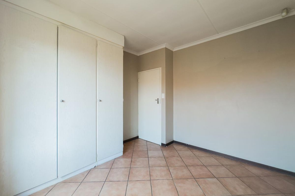 A vacant bedroom featuring built-in cupboards, neutral wall tones, and tiled flooring, offering a clean and versatile space ready for personalization.