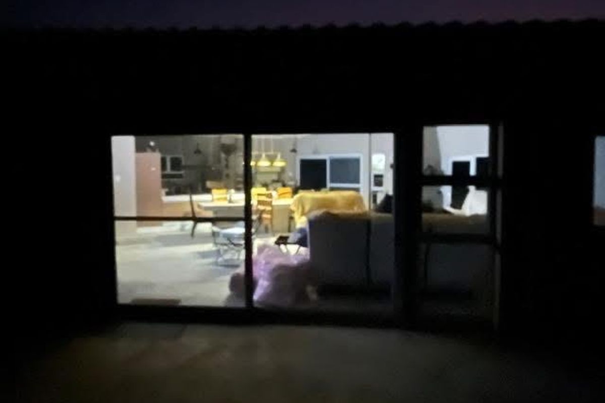 A night view looking through large sliding glass doors into an open-plan living and kitchen area.