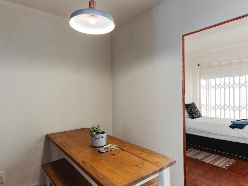 A dining area featuring a pendant light and wooden parquet flooring, with a view into an adjacent bedroom through a doorway.