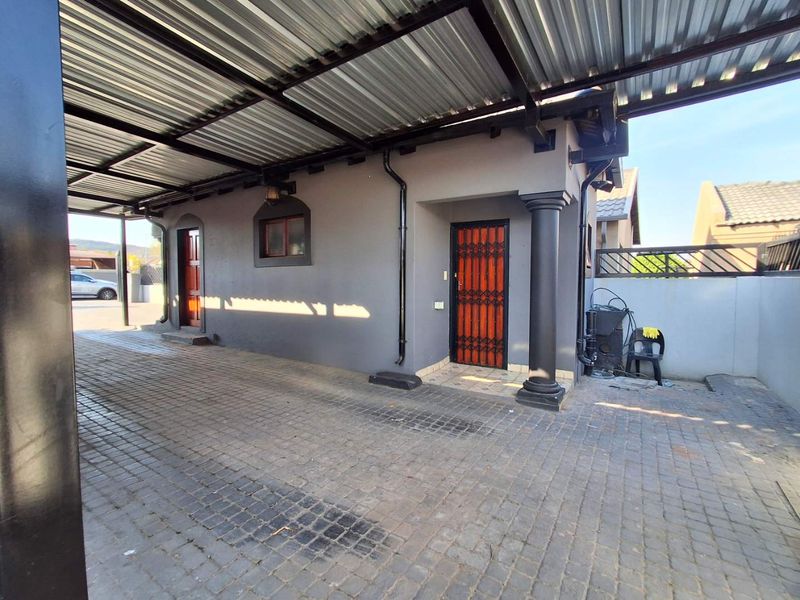 A covered paved driveway and entrance area featuring a corrugated metal roof, security gates, and a structural pillar.