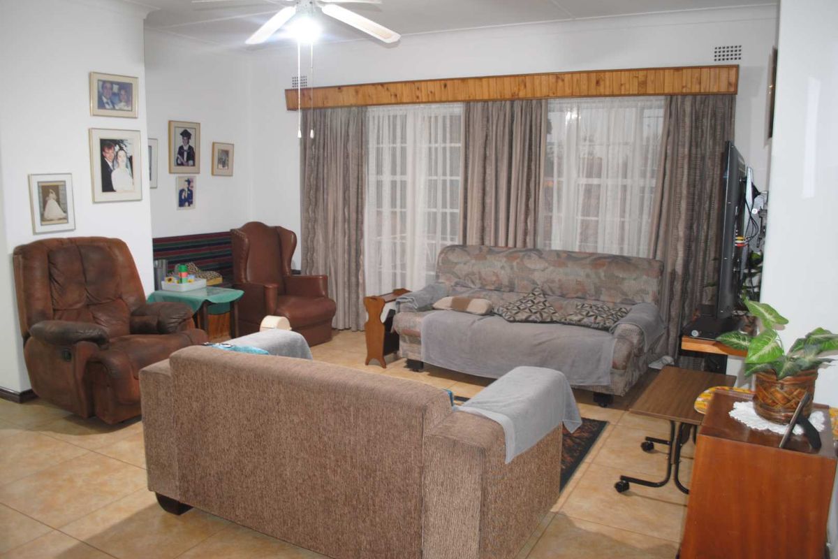 A comfortable living room featuring tiled flooring, a ceiling fan, and large windows with wooden pelmets, offering a functional and lived-in space.