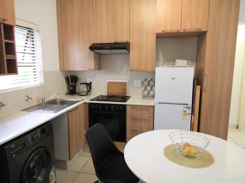 Compact kitchen featuring light wood-finish cabinetry, laminate countertops, integrated oven and hob, and tiled flooring, offering a functional and well-maintained cooking space.
