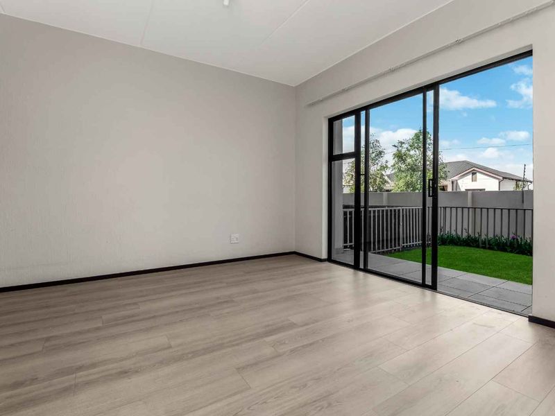 Bright and spacious living area featuring modern laminate flooring and large sliding glass doors that open onto a private patio and garden.