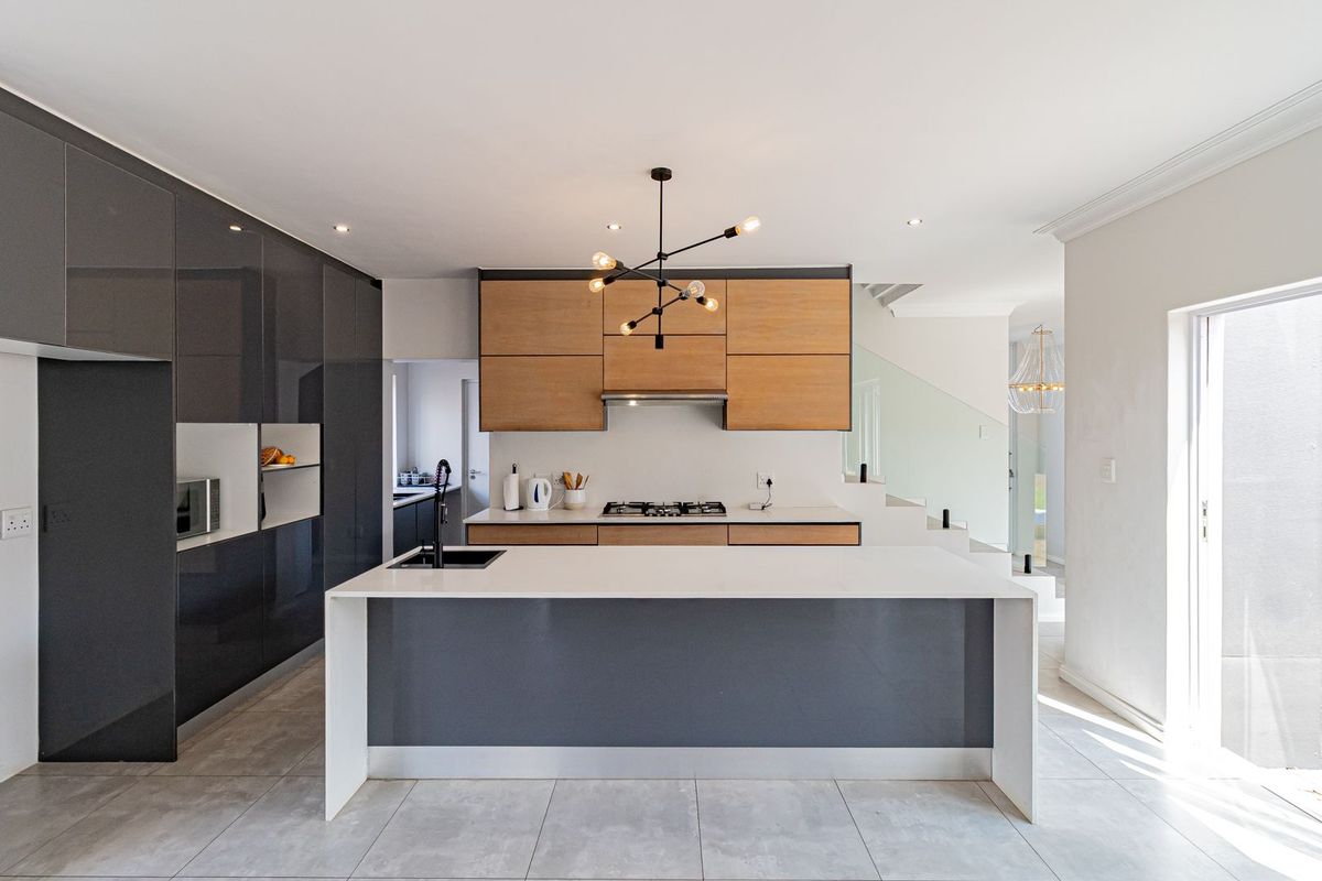 Modern kitchen featuring a central island with a sink, high-gloss cabinetry, wood-tone upper cabinets, integrated gas hob, and sleek tiled flooring.