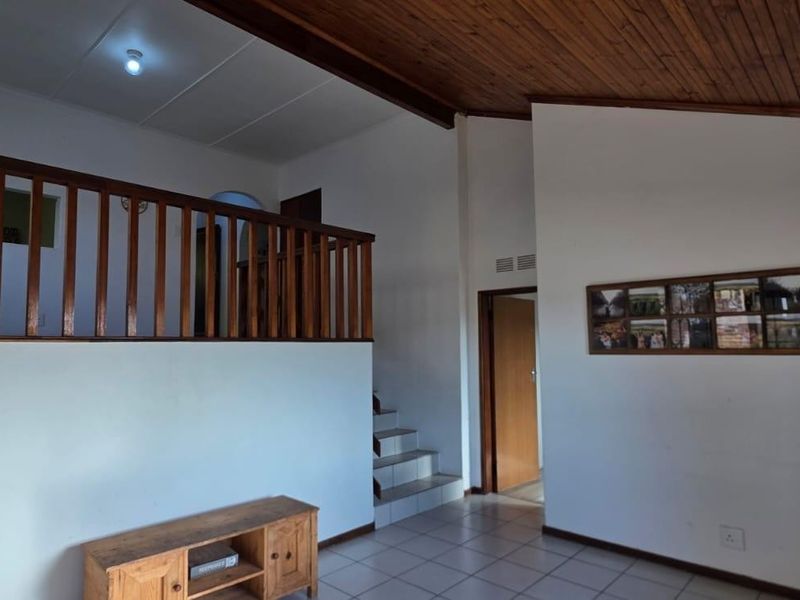 Spacious living area featuring a high timber raked ceiling, tiled flooring, and a wooden balustrade overlooking the lower level.
