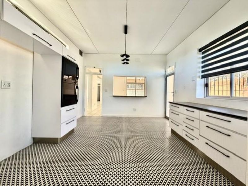 A bright, modern kitchen featuring white cabinetry, built-in oven, patterned floor tiles, and a convenient pass-through window to the adjacent living area.