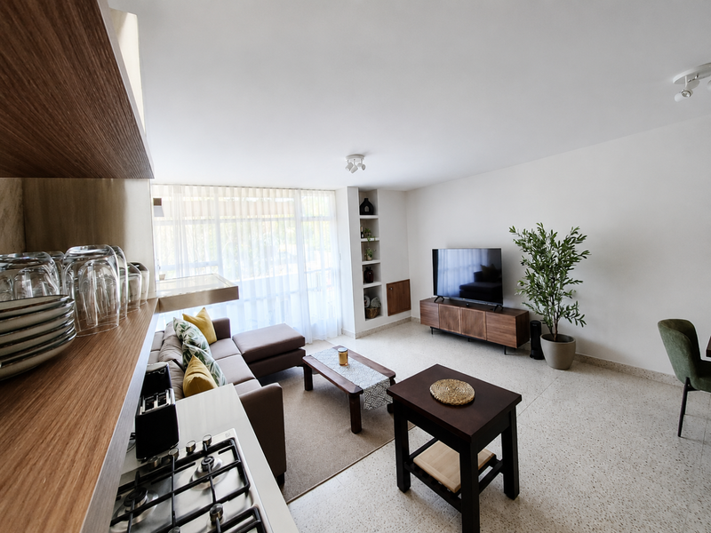 Bright open-plan living area featuring terrazzo flooring, built-in wall shelving, and a modern kitchen corner with a gas cooktop.