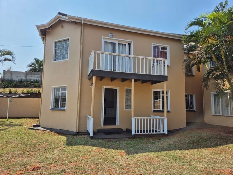 Rear view of a two-story townhouse featuring a ground-floor patio, an upper-level balcony with railings, and a private garden area.