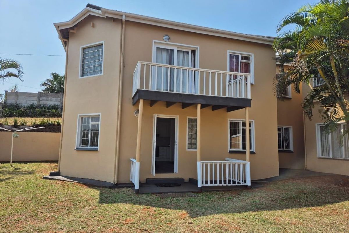 Rear view of a two-story townhouse featuring a ground-floor patio, an upper-level balcony with railings, and a private garden area.