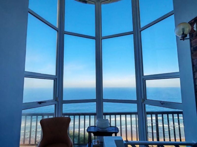 A bright living space featuring a large bay window with expansive ocean views and a balcony railing.