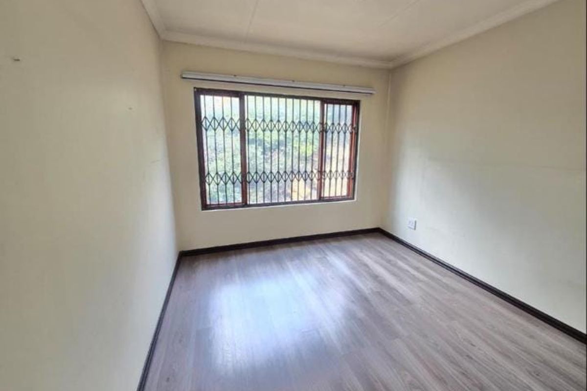 A vacant bedroom featuring modern laminate flooring, neutral walls, and security bars on the window, providing a clean canvas for personalization.