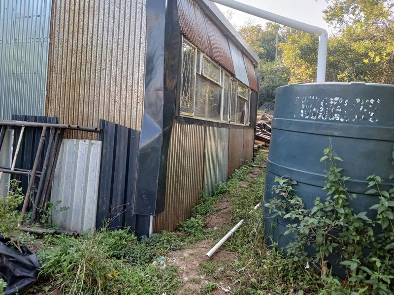 Rear view of a structure featuring corrugated metal cladding, a water storage tank, and visible signs of weathering and corrosion.