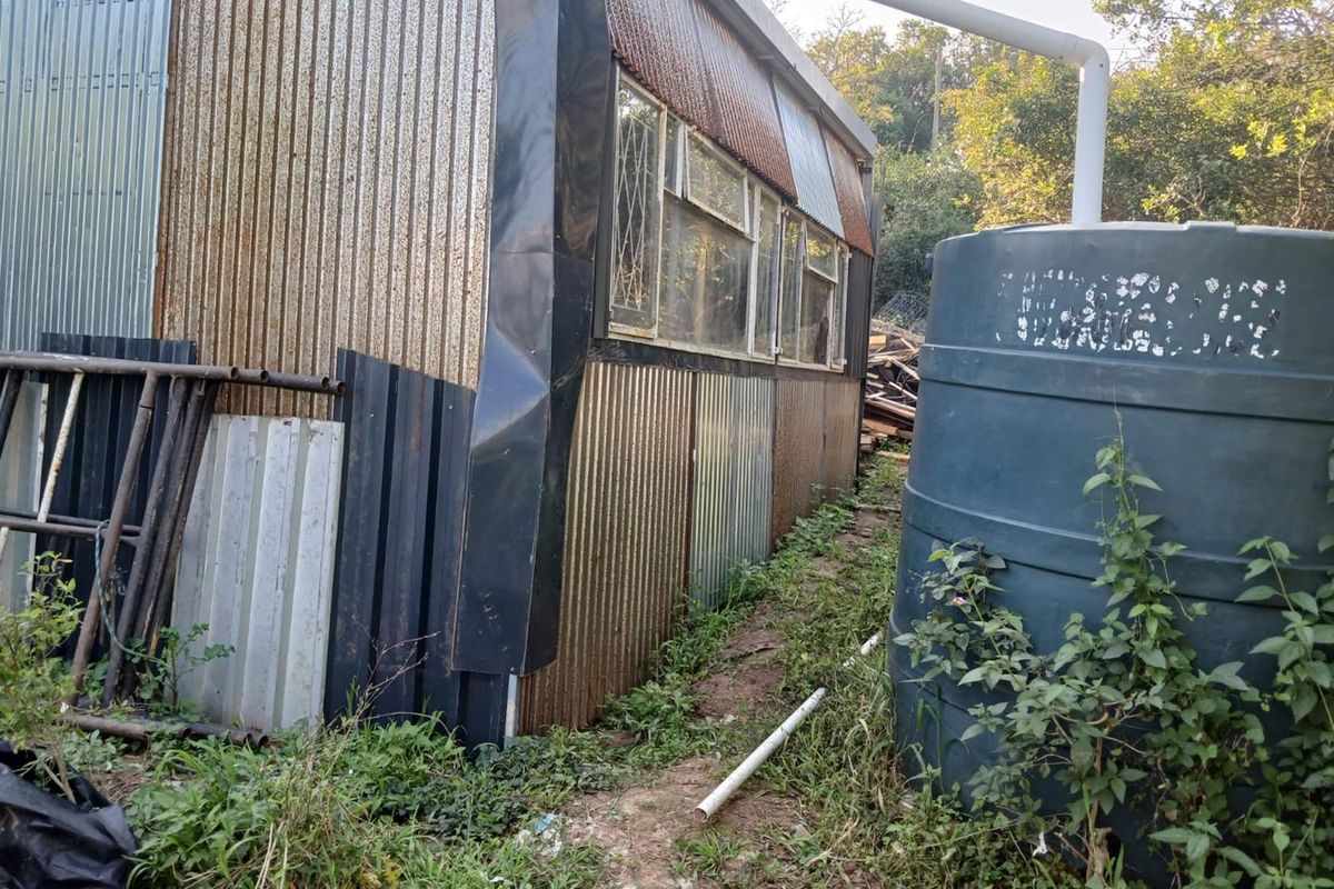 Rear view of a structure featuring corrugated metal cladding, a water storage tank, and visible signs of weathering and corrosion.