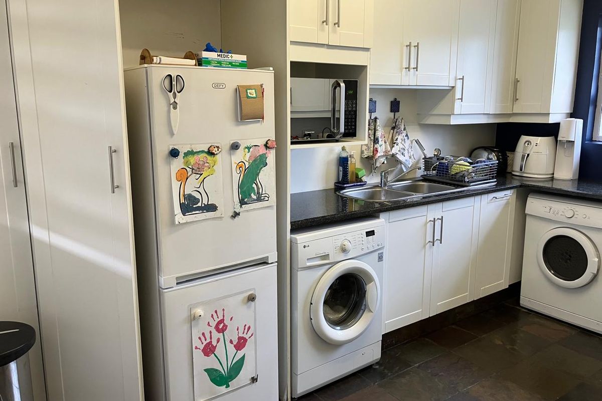 A functional kitchen featuring white cabinetry, dark stone countertops, slate flooring, and integrated laundry appliances, providing a practical workspace for daily tasks.
