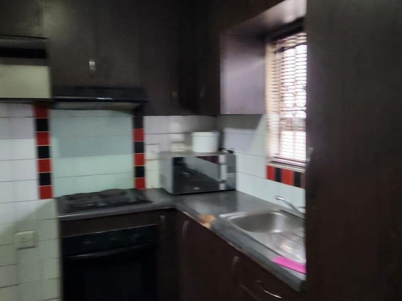 Compact kitchen featuring dark cabinetry, built-in oven, hob, and extractor fan, requiring ceiling repairs and cosmetic updates to improve functionality and aesthetic appeal.