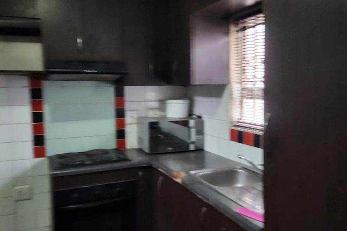 Compact kitchen featuring dark cabinetry, built-in oven, hob, and extractor fan, requiring ceiling repairs and cosmetic updates to improve functionality and aesthetic appeal.