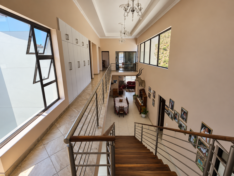 Spacious upper-level hallway featuring built-in storage cabinetry, a modern staircase with stainless steel balustrades, and large windows overlooking the lower living area.