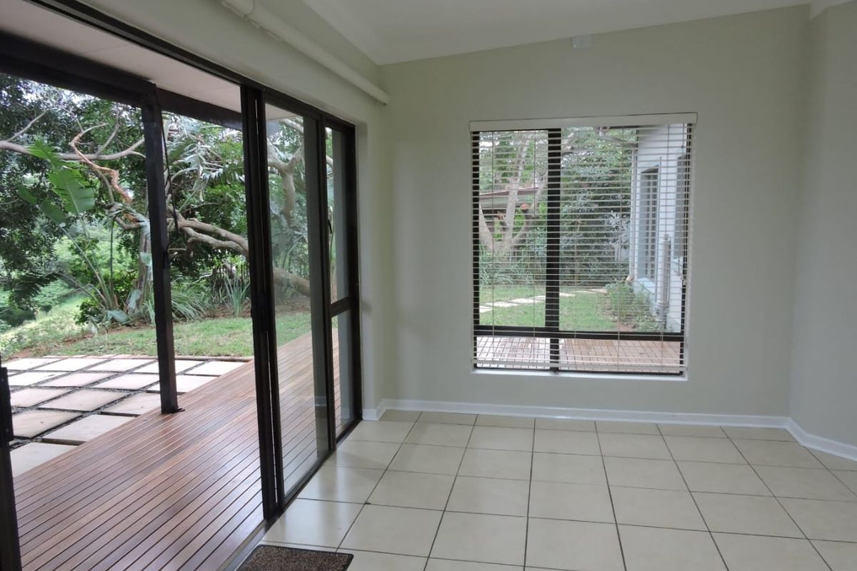 Bright and spacious living area featuring large sliding glass doors that open onto a wooden deck, with neutral tiled flooring and garden views.