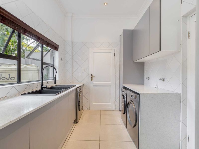 Modern, well-appointed laundry room featuring sleek grey cabinetry, stone countertops, a double basin sink, and dedicated space for laundry appliances.