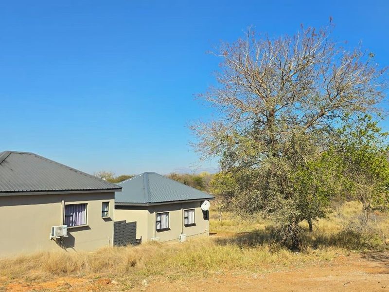 Rear view of the property showing the metal roof, exterior walls, and installed air conditioning units set within a natural landscape.