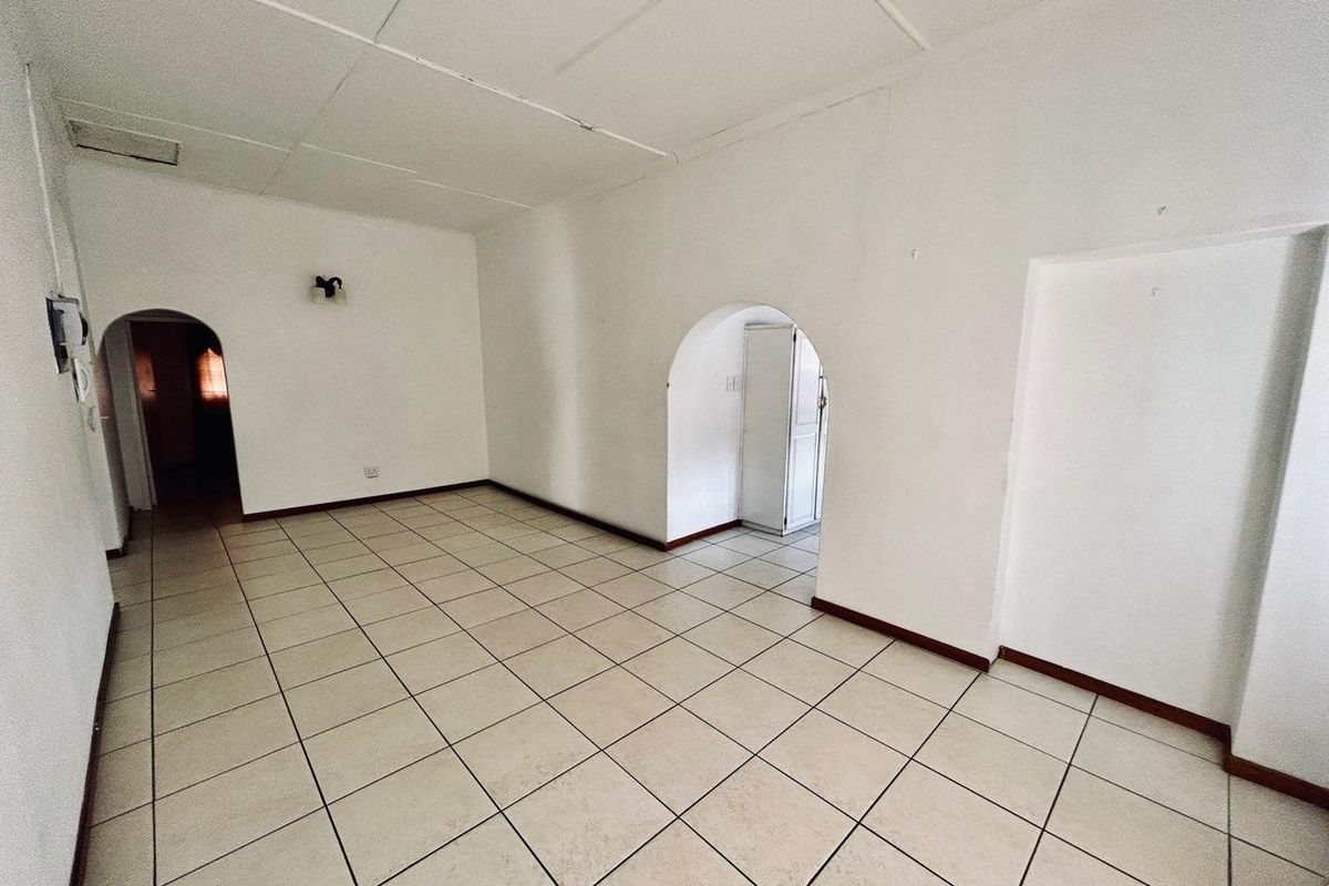 An empty living area featuring tiled flooring, arched doorways, and a drop ceiling, providing a blank canvas for renovation.
