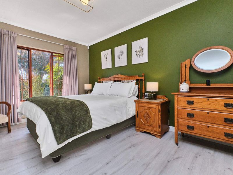 A well-maintained bedroom featuring laminate flooring, a feature green wall, and a timber-framed sliding door providing access to the garden.