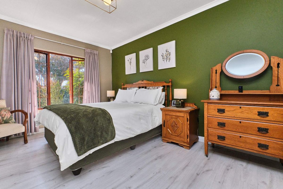 A well-maintained bedroom featuring laminate flooring, a feature green wall, and a timber-framed sliding door providing access to the garden.