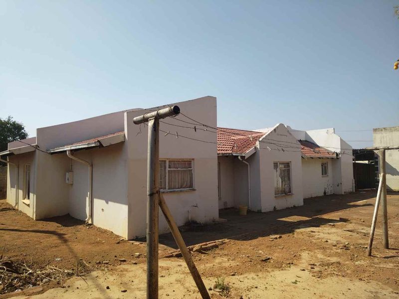 Rear view of a single-story house featuring a tiled roof and metal window frames, showing signs of exterior wear and unmaintained grounds.