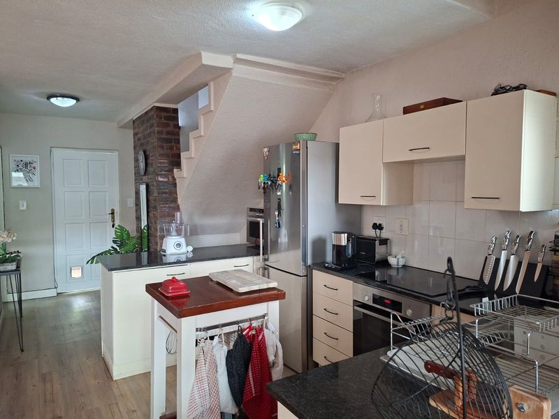 Compact kitchen featuring built-in cabinetry, granite countertops, and an integrated oven and hob, set against an exposed brick feature wall and staircase.