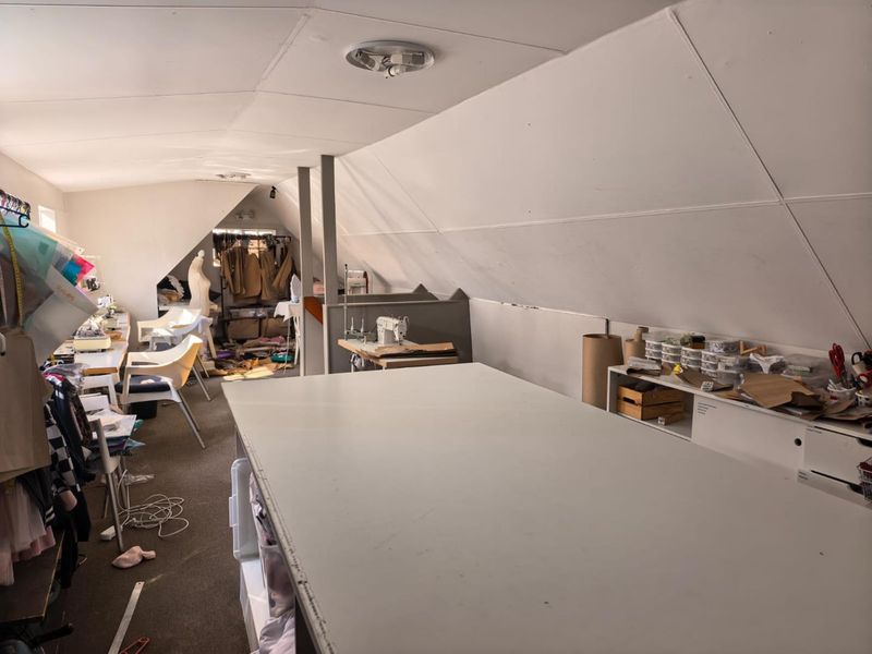 An attic-style office space featuring sloped ceilings, built-in shelving, and ample workspace, suitable for a creative studio or professional office environment.