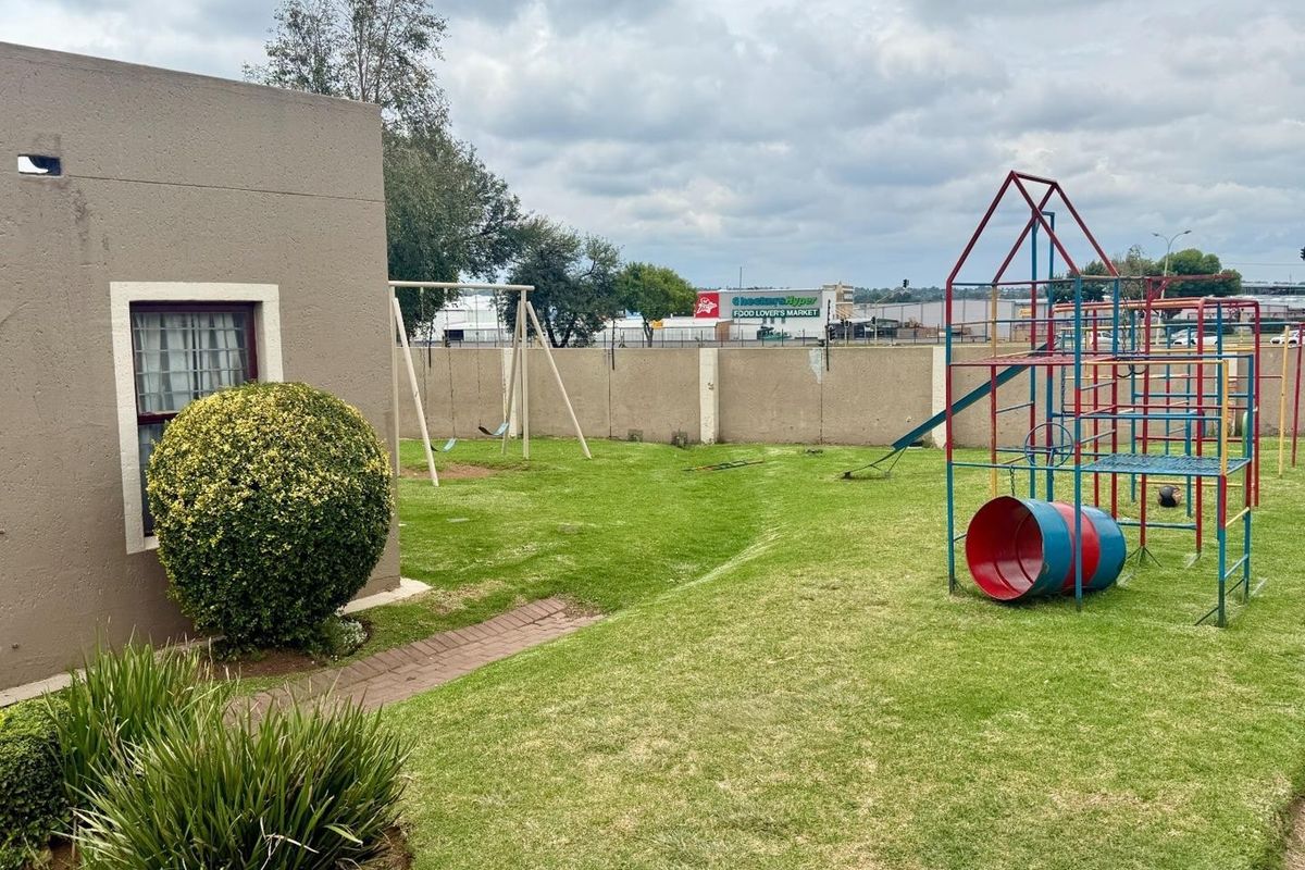 A private rear garden area featuring a lawn, paved walkway, and a playground structure, enclosed by a perimeter boundary wall.