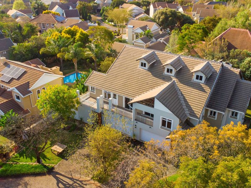 Aerial view of a residential property featuring a tiled roof with dormer windows, solar panels, a balcony, and a private swimming pool.