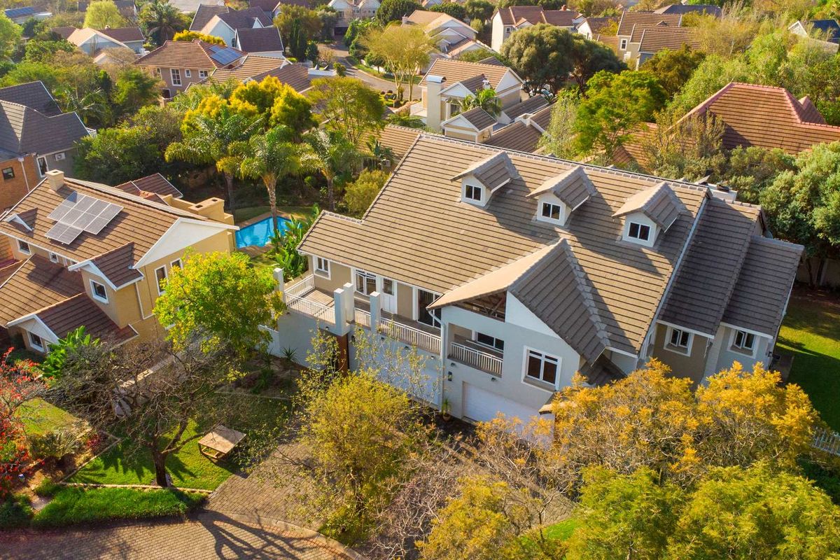 Aerial view of a residential property featuring a tiled roof with dormer windows, solar panels, a balcony, and a private swimming pool.