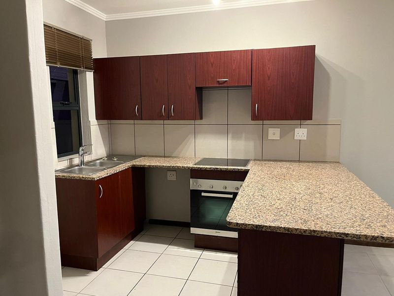 A functional kitchen featuring dark wood-look cabinetry, granite countertops, a built-in oven with electric hob, and tiled flooring.