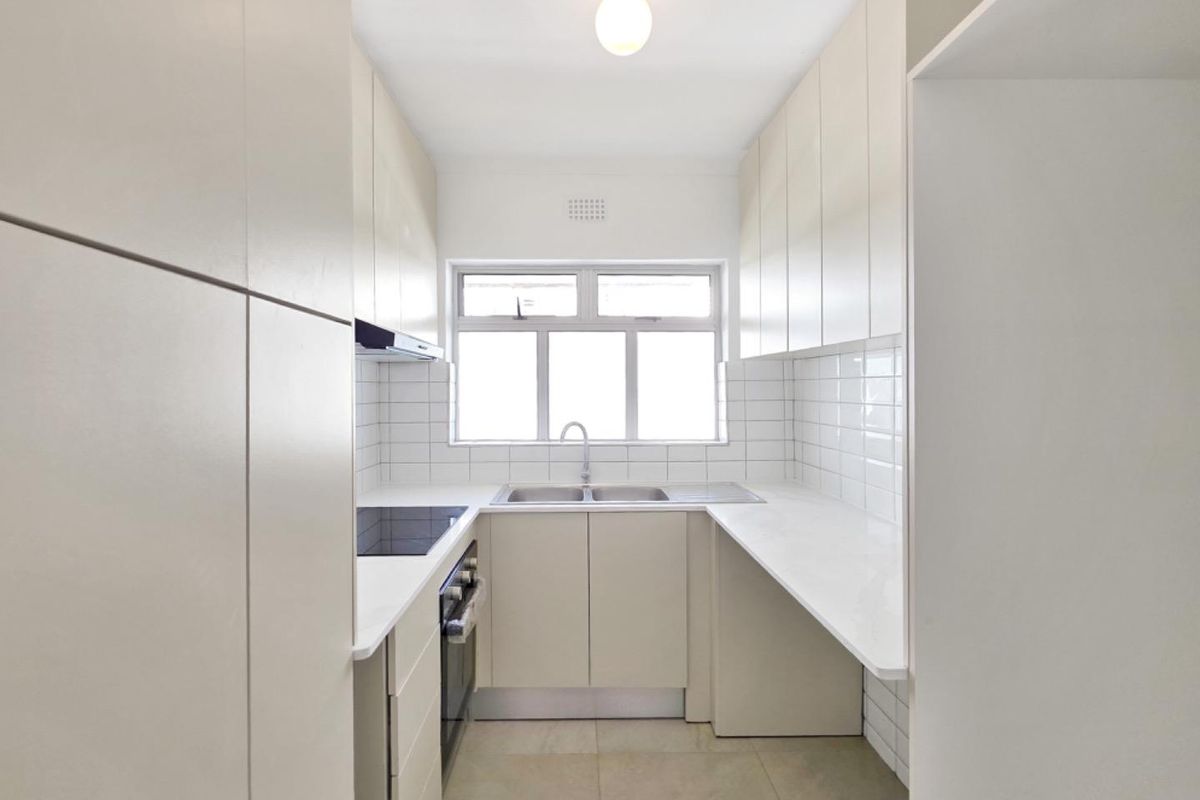 A clean, modern galley-style kitchen featuring white cabinetry, stone countertops, subway tile backsplash, and integrated stainless steel appliances.