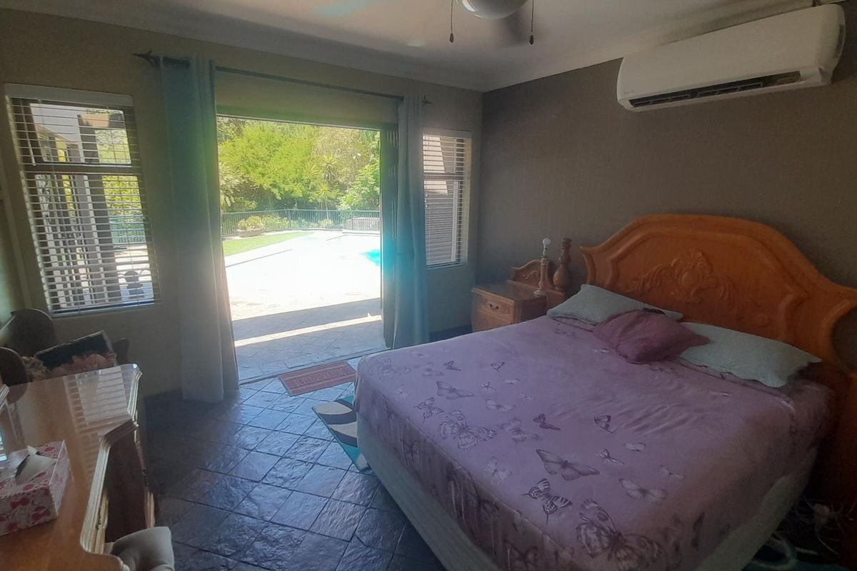 Spacious bedroom featuring tiled flooring, a wall-mounted air conditioning unit, and direct access to the outdoor pool area through sliding glass doors.