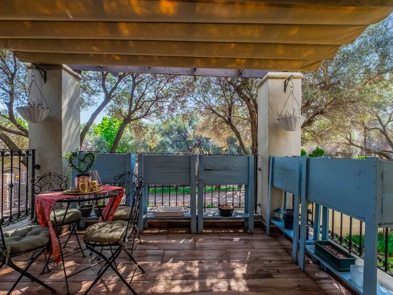 A covered balcony featuring timber-look decking, wrought iron railings, and a retractable awning, offering a pleasant outdoor space with garden views.