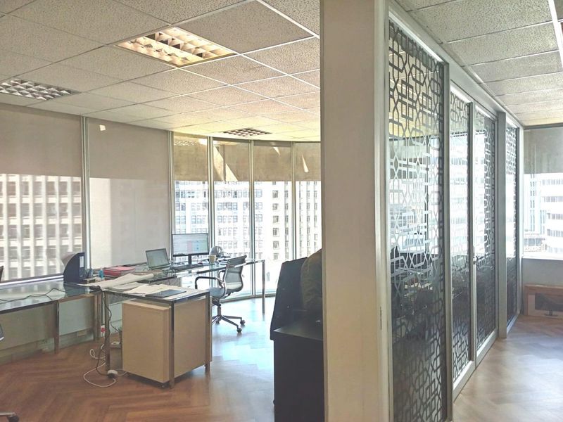 Modern office space featuring parquet flooring, suspended ceilings, and decorative glass partitions with expansive city views through floor-to-ceiling windows.