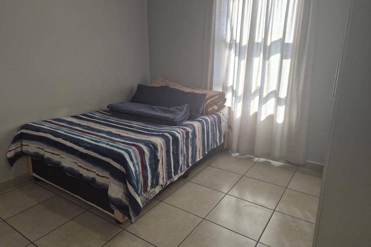A bedroom featuring tiled flooring and a window with curtains, providing natural light to the space.
