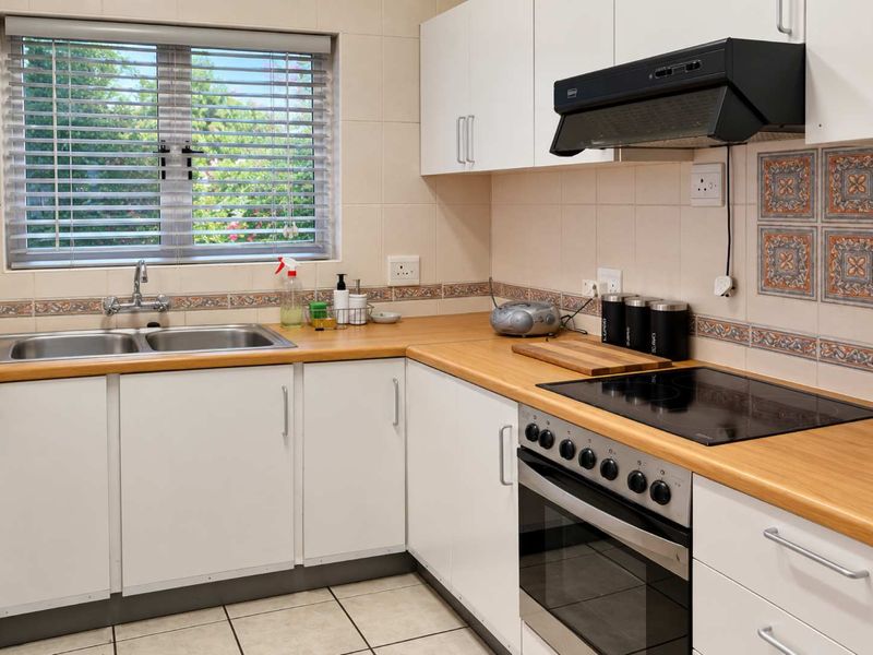 Functional kitchen featuring white cabinetry, wood-look laminate countertops, a built-in oven with hob, and a stainless steel double sink with tiled backsplash.