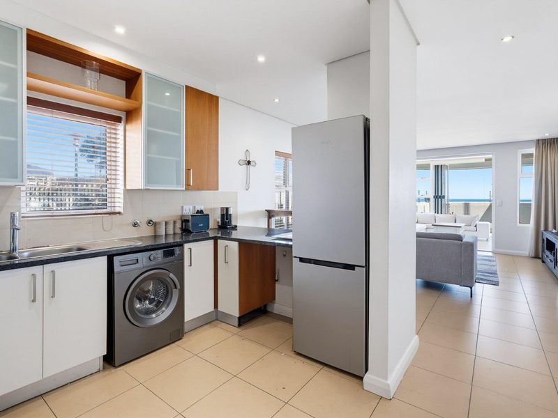 Modern open-plan kitchen featuring sleek cabinetry, granite countertops, and integrated laundry facilities, flowing seamlessly into a bright living area with balcony access.