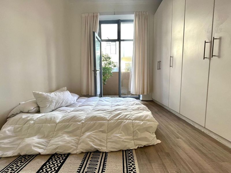 A bright bedroom featuring built-in cupboards, laminate flooring, and direct access to a private balcony through a glass door.