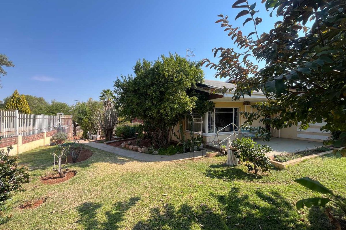 A view of the rear exterior of the house featuring a covered patio, paved walkway, and a well-established garden with perimeter fencing.