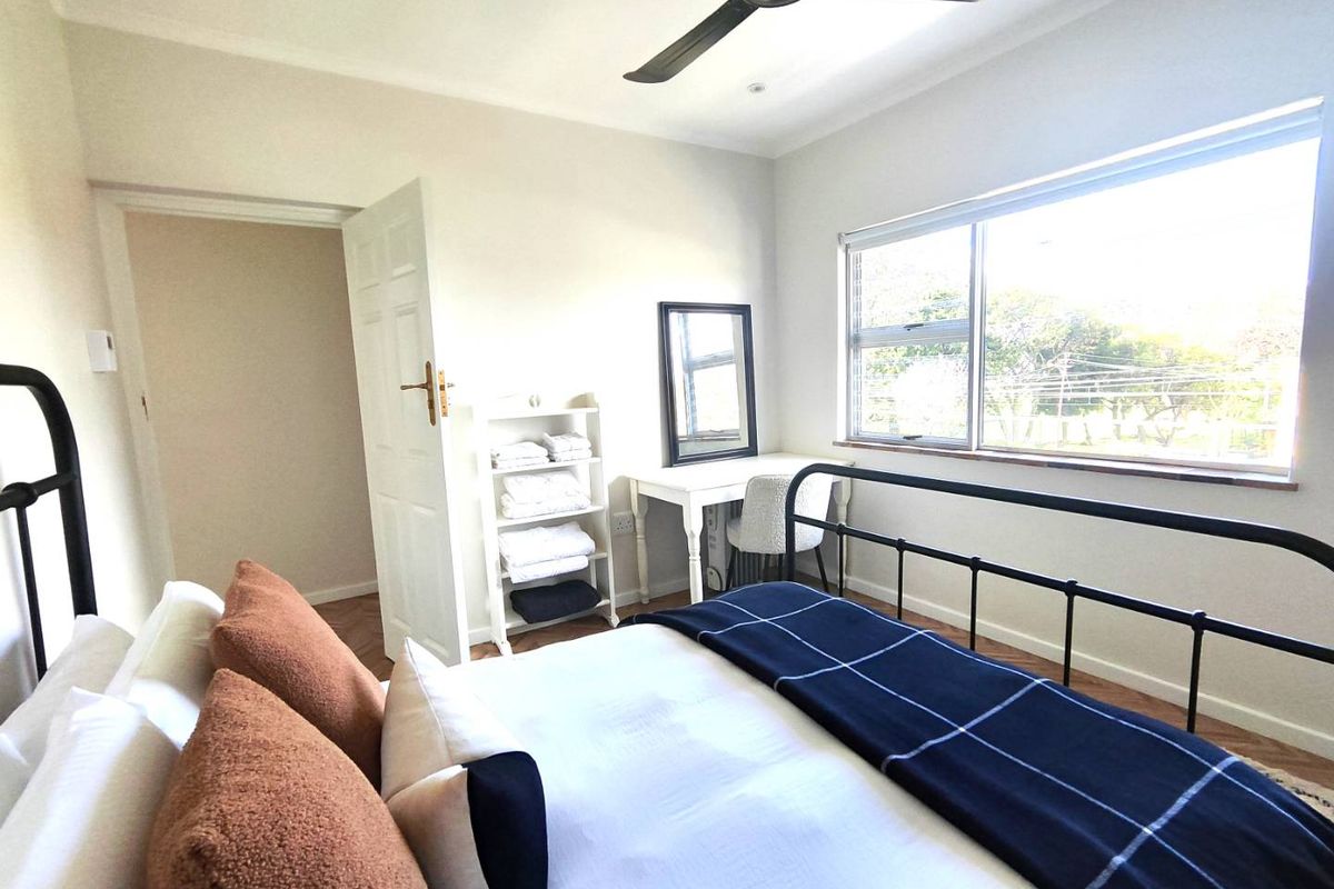 A bright bedroom featuring timber flooring, a ceiling fan, and large windows providing natural light.